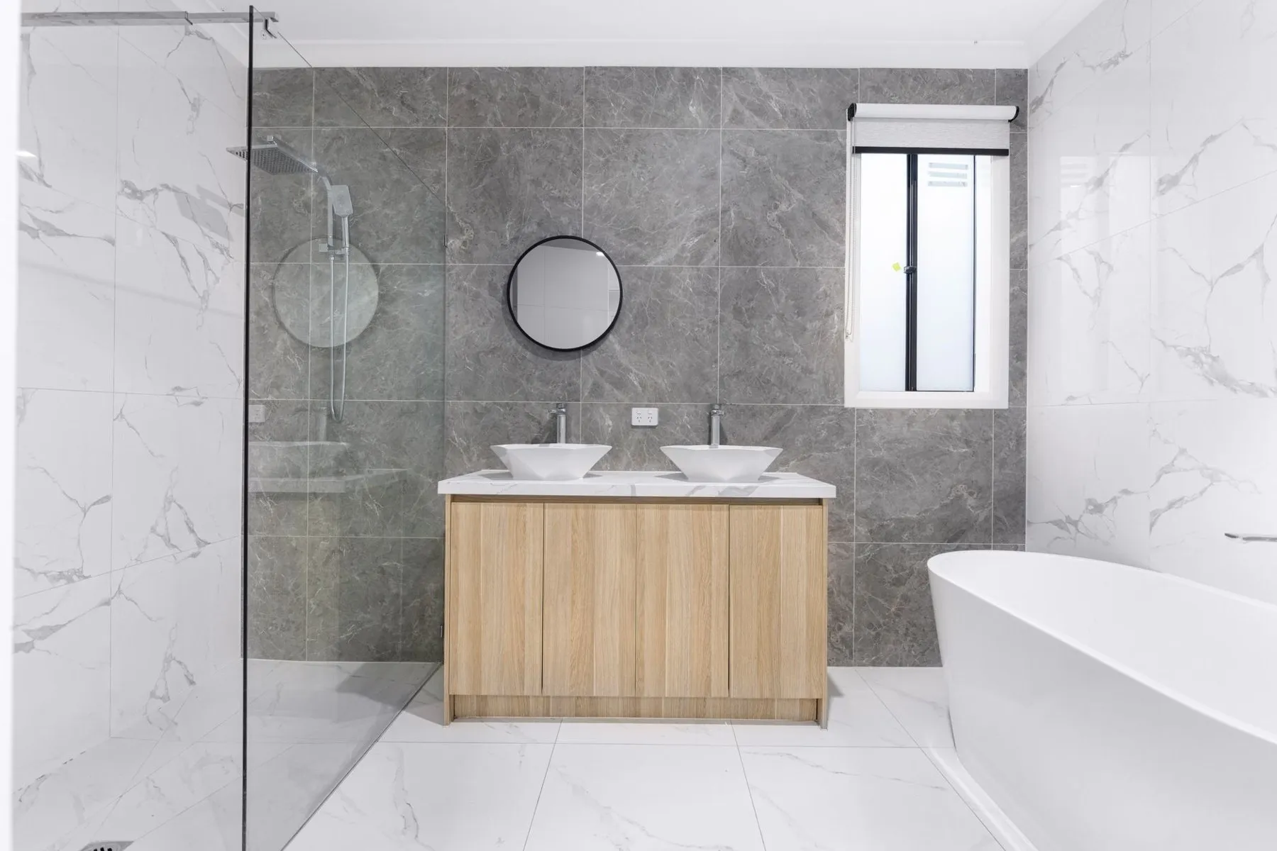 A finished bathroom with grey marble-effect tiles, two basins on a timber vanity and a freestanding bath