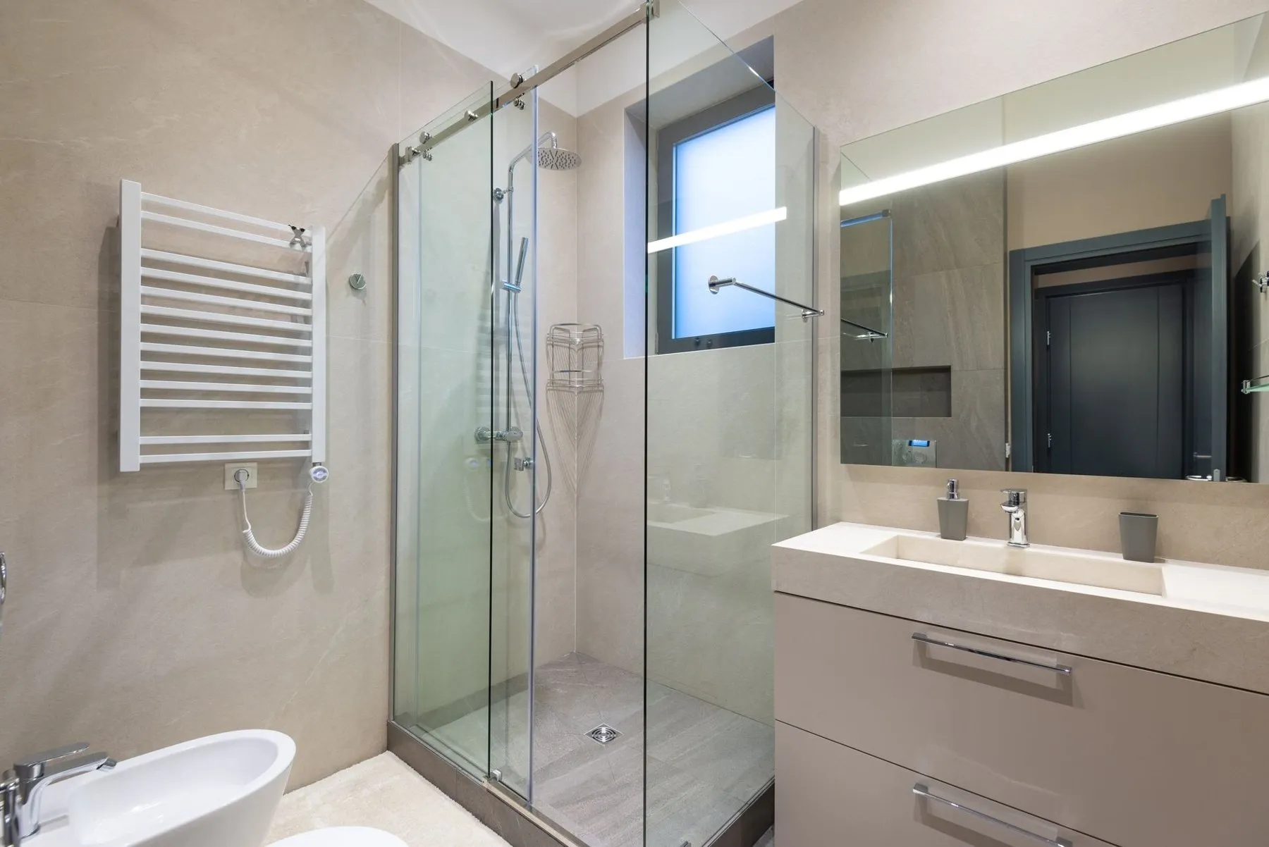 A finished shower room with a glass sliding enclosure, towel radiator and stone vanity