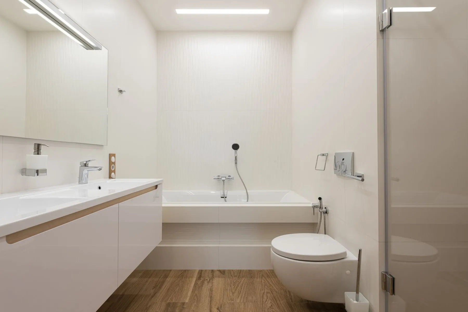 A bright finished bathroom with a white vanity, bath and wall-hung toilet