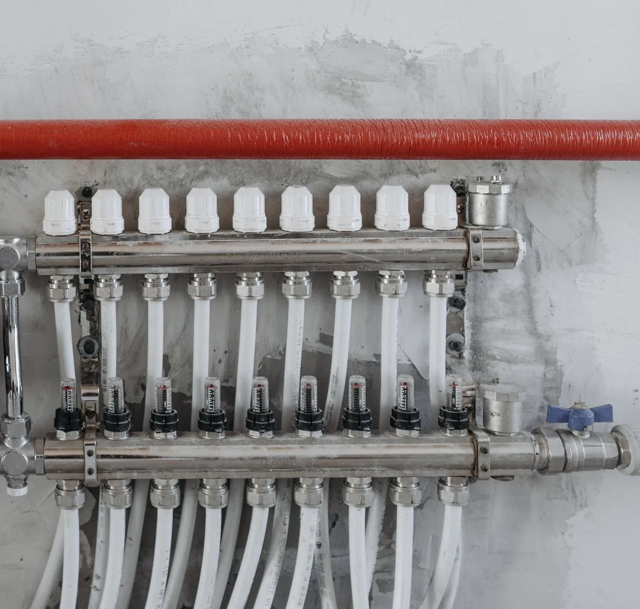 A heating manifold with a pump, gauges and white pipes fixed to a plastered wall