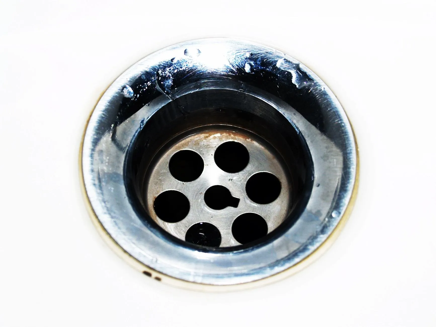 A close-up of a chrome plughole in a white basin