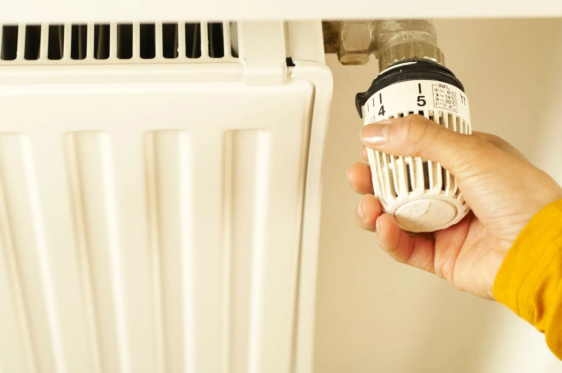 A hand turning a thermostatic radiator valve on a white radiator