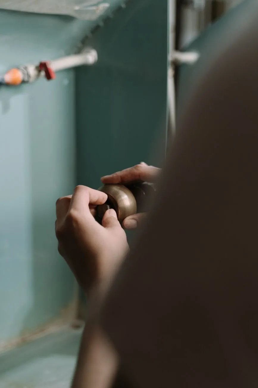 An engineer's hands tightening a brass fitting inside a sink cabinet