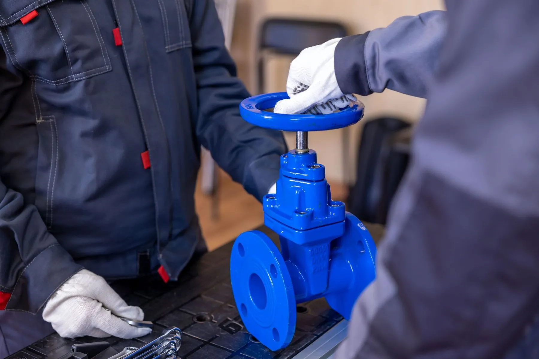 Two engineers in navy workwear fitting a new blue gate valve on the bench